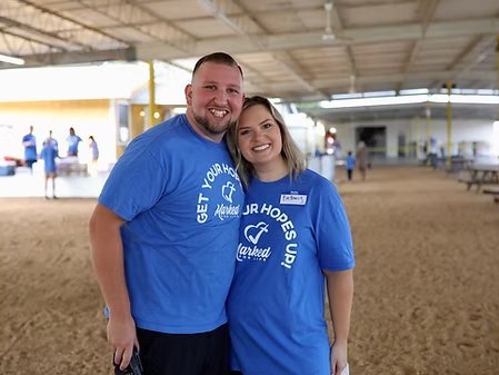 Two Marked For Life volunteers in blue Your Hopes Up shirts smiling at an indoor outreach event