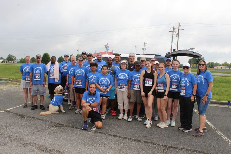 About thirty Freedom Run participants in blue Marked For Life shirts pose with race bibs, along with a dog in a matching shirt.