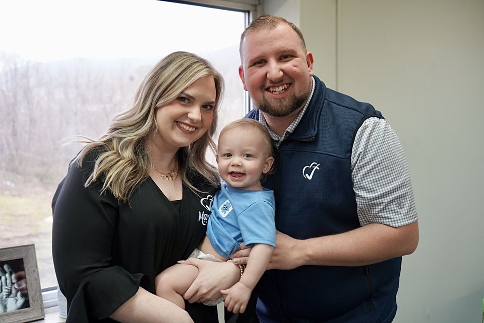Logan and Brittany LeGrande hold their son in front of an office window.