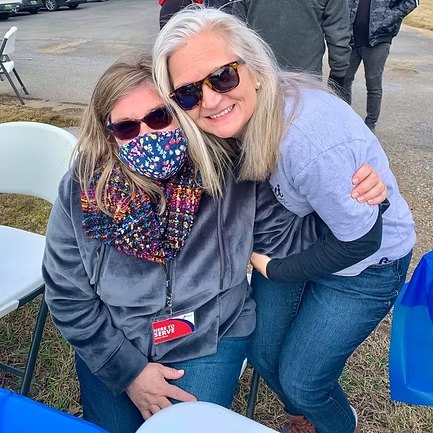 Two volunteers hugging at an outdoor Deliver Hope table