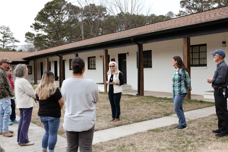 A staff member leads a group of new volunteers along the white porch of the Hope House during a campus tour.