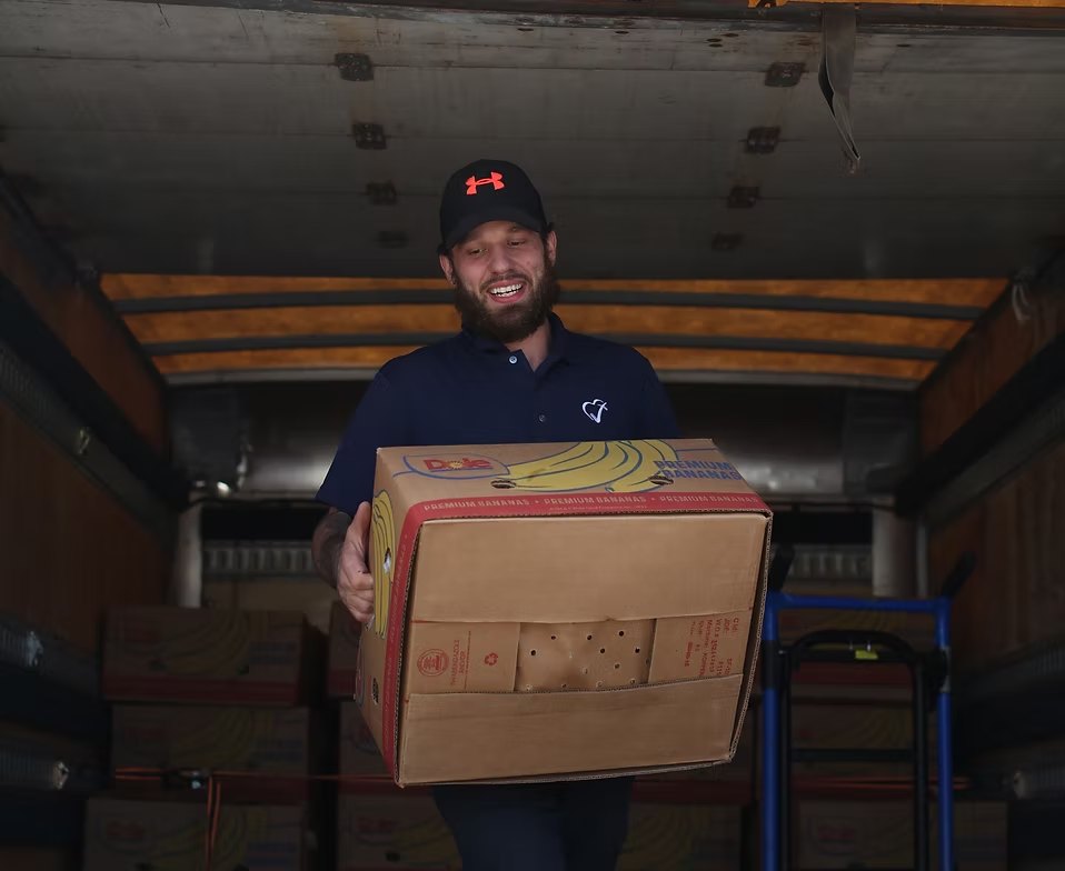 Volunteer smiling while carrying a box of bananas out of a delivery truck