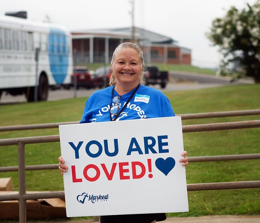 Volunteer holding a sign that reads You Are Loved